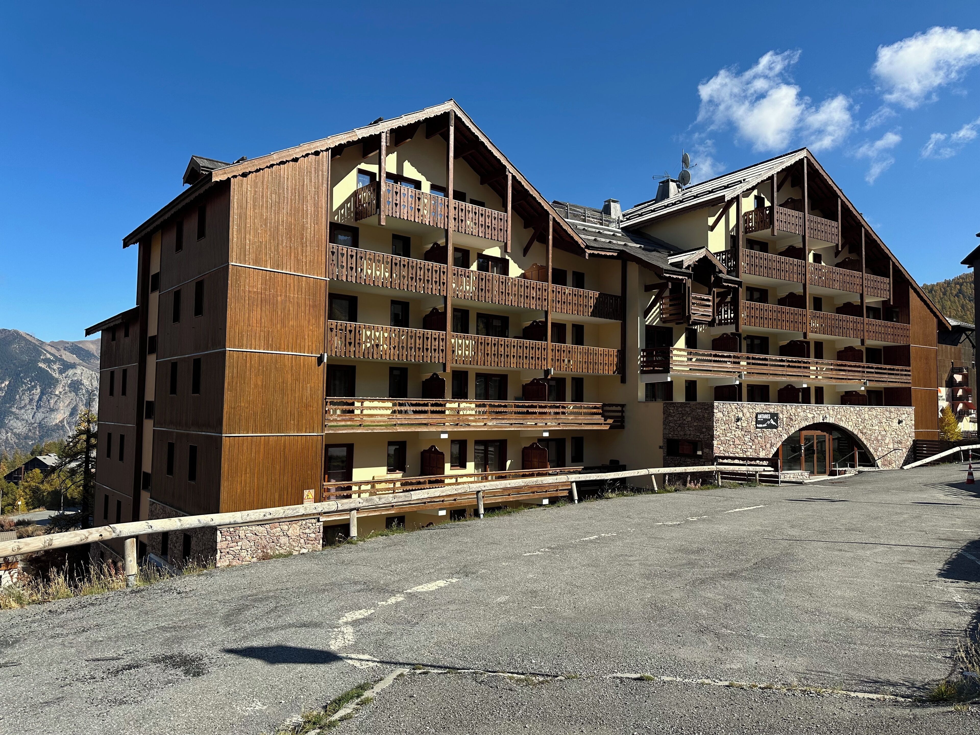 A multi-story hotel with balconies, a stone facade, and a mountainous backdrop.