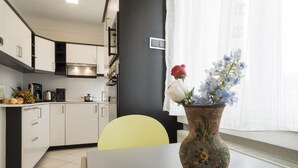 Una cocina moderna con armarios blancos, una silla amarilla y un jarrón con flores sobre una mesa.