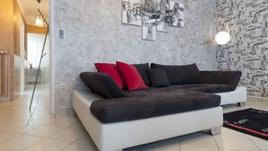 Un salón moderno con un sofá blanco, cojines rojos y negros, una araña y un papel tapiz estampado.