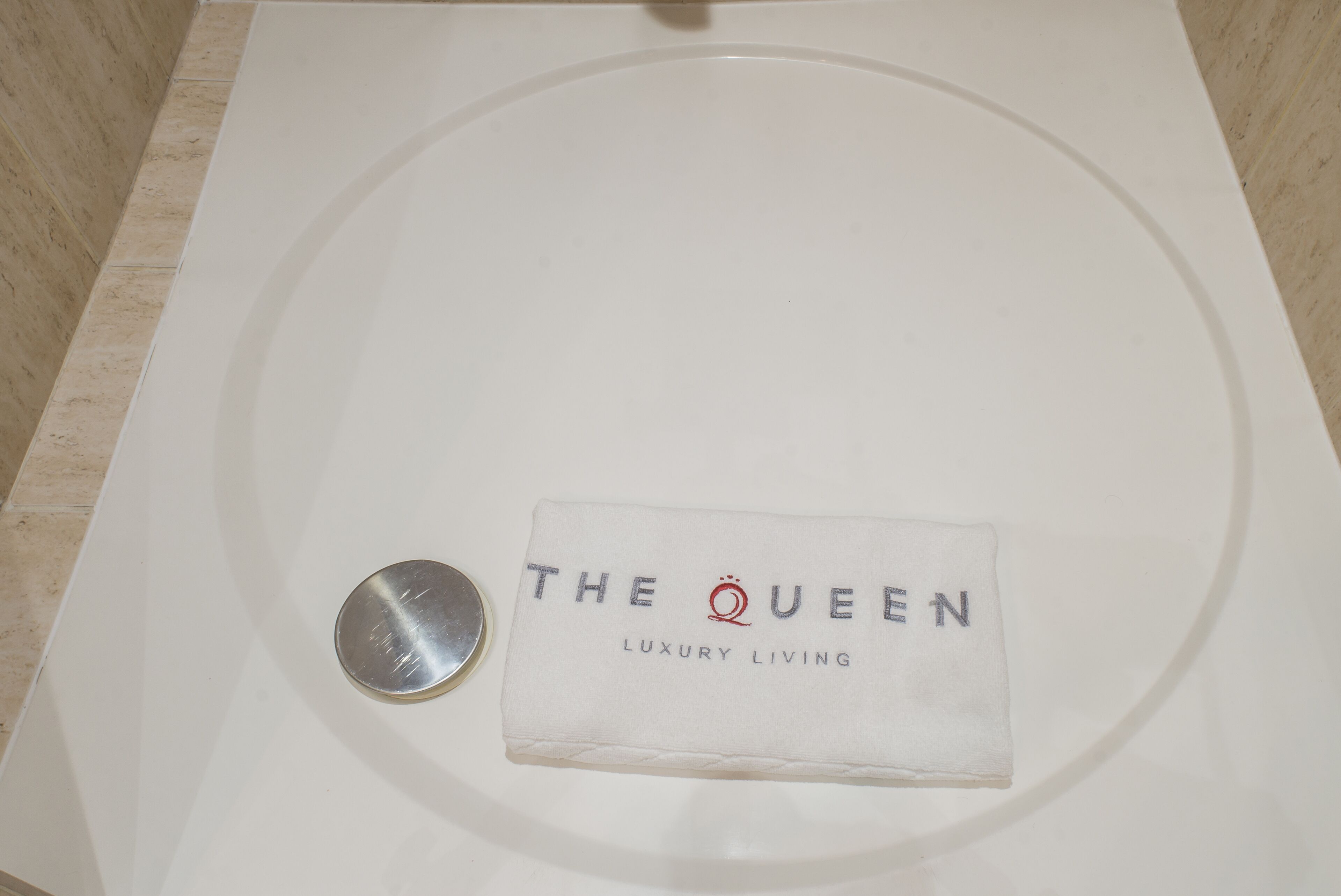 A white bathtub with a towel labeled "THE QUEEN LUXURY LIVING" and a small metallic object beside it.