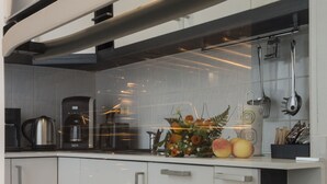 Una cocina moderna con armarios blancos, electrodomésticos de acero inoxidable y una encimera con frutas y un florero.