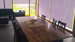 A dining area with a large wooden table, black chairs, and a small stool. There is a ceiling fan and a window with a view of the outdoors. - Refugio, Castelo de Paiva (Pedorido)