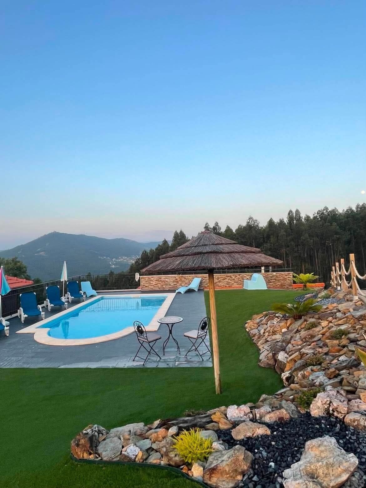 A swimming pool with lounge chairs and a thatched umbrella, surrounded by a landscaped garden with a view of distant mountains.