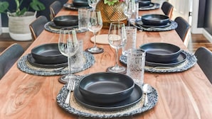 Una mesa de comedor de madera vestida con platos negros, vasos transparentes y un jarrón decorativo con flores rosadas.