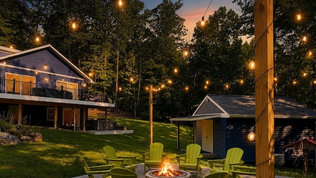 Una terraza con sillas verdes y una chimenea, rodeada de una casa y árboles.