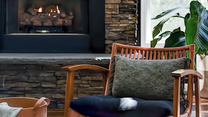 Un salón acogedor con chimenea de piedra, un sillón de madera cómodo y un ventanal grande.