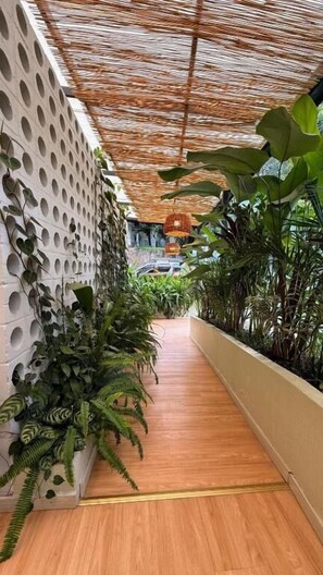 A corridor with a wooden floor, a perforated wall on one side, and a variety of plants on both sides. - Muuk Boutique Hotel Campestre (Medellín)