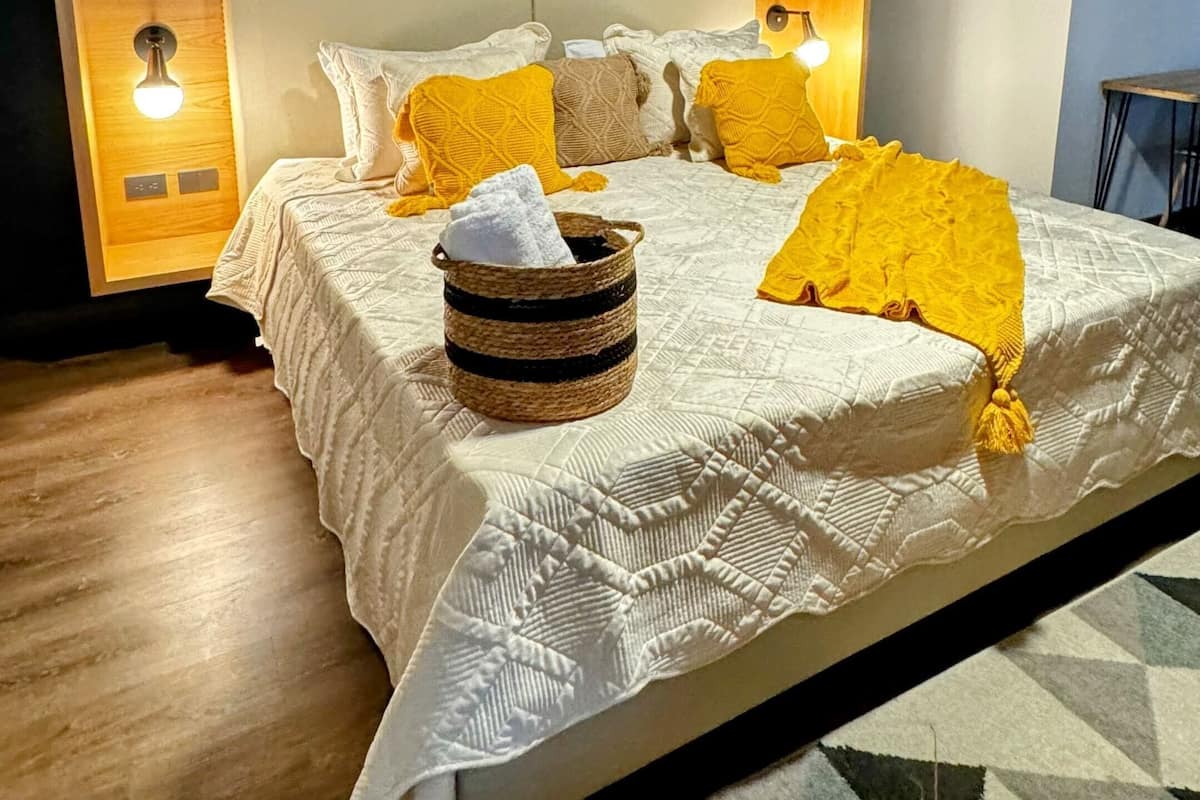 A bedroom with a wooden ceiling, a bed with white and yellow bedding, and two bedside lamps.