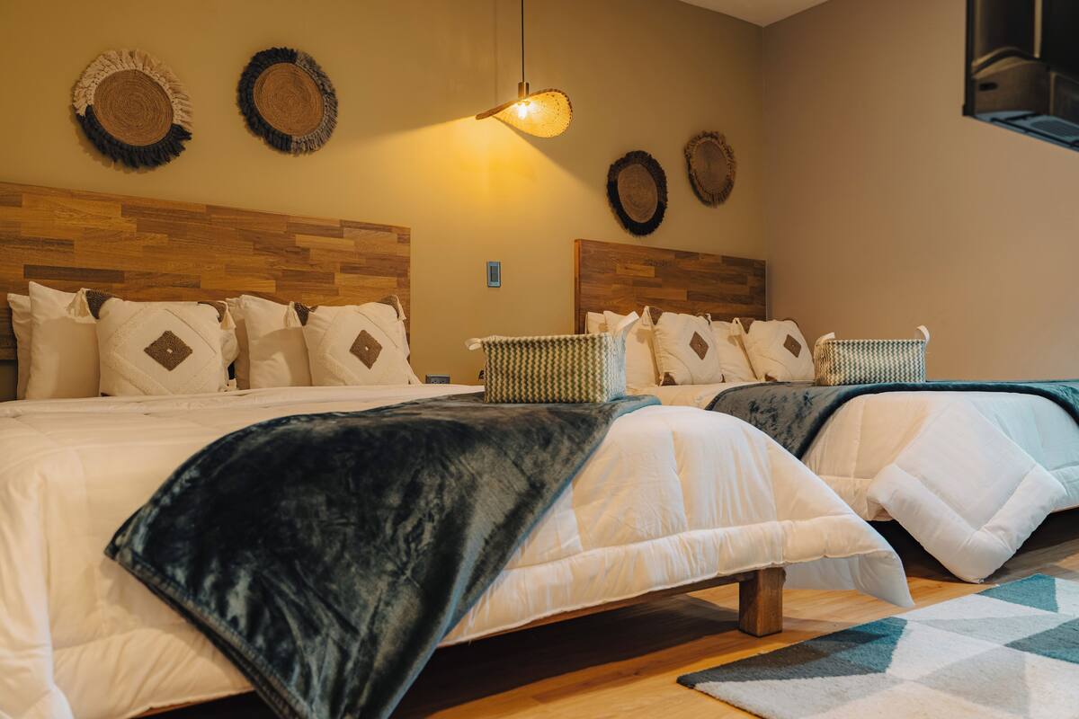 A hotel room with two beds, a wooden headboard, woven baskets, and a geometric rug.