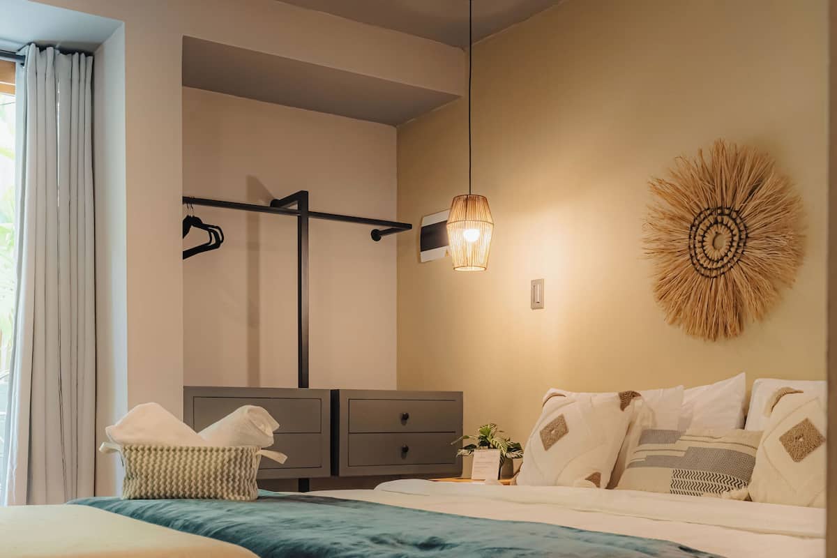 A bedroom with a bed, bedside tables, a bench, a hanging light fixture, and a wall decoration.