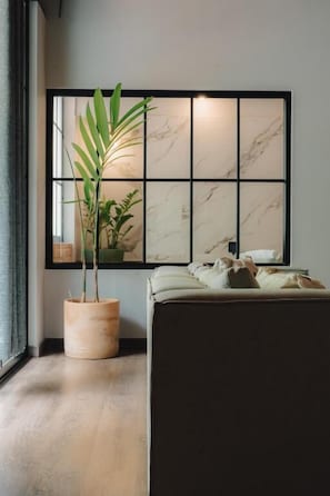 Ein Zimmer mit einem großen Fenster, einem Blumentopf, einem Sofa und einer Wand mit Rillenmuster.