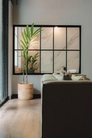 Una habitación con un ventanal grande, una planta en maceta, un sofá y una pared con diseño de cuadrícula.