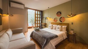 A bedroom with a bed, a sofa, a small table, and a window with a view. - Muuk Boutique Hotel Campestre (Medellín)