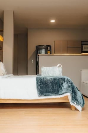 Ein Schlafzimmer mit einem Bett, einem Nachttisch und einer kleinen Küchenzeile inklusive Mikrowelle und Kaffeemaschine.
