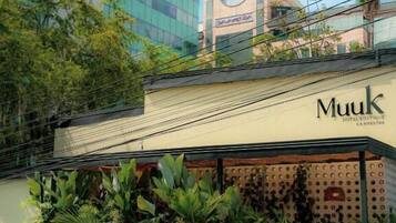A hotel named 'Muuk' with a modern facade, a covered entrance, and lush greenery in front.