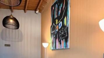 A modern living room with a black leather sofa, a large abstract painting, and pendant lighting.