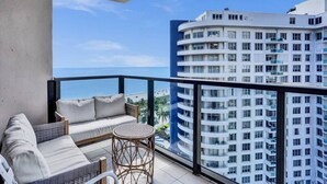A balcony with a sofa, chairs, and a small table, overlooking a high-rise building and the ocean. - High Floor Beachfront Condo / Beach Service / 1509 (Miami Beach)