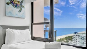 A hotel room with a bed, a window with a view of the beach and ocean, and a painting of a turtle on the wall. - Ocean View Retreat / Beach Service / 1603 (Miami Beach)
