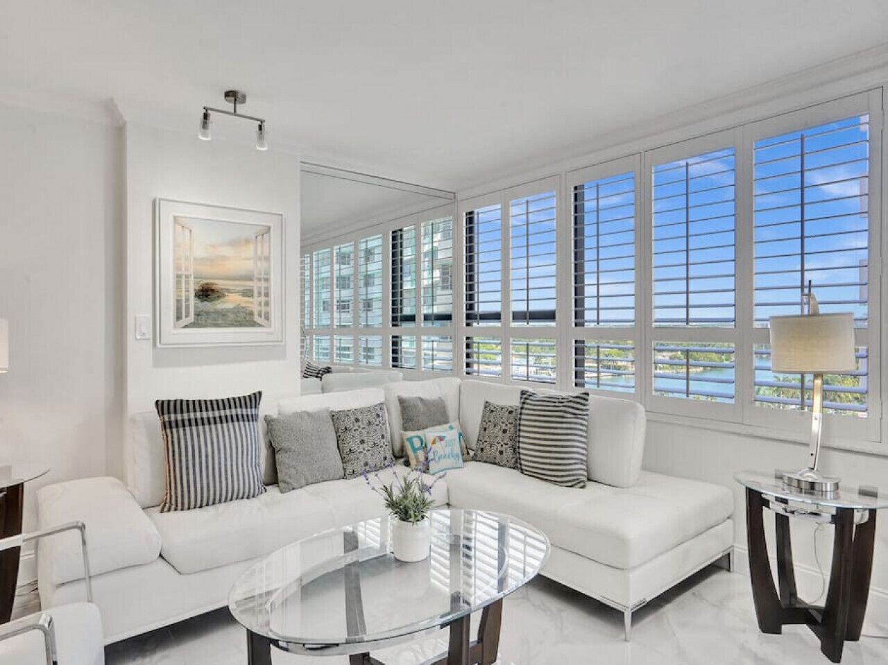 A modern living room with a white sofa, a glass coffee table, and a view of the sea through large windows.