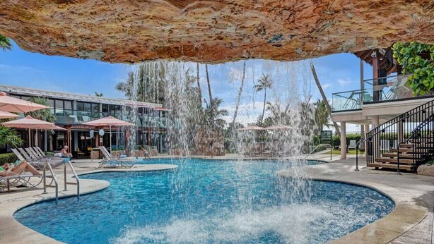 A pool area with a water feature, lounge chairs, and a covered seating area. - Ocean View Condo / Beach Service & Pool / 618 (Miami Beach)