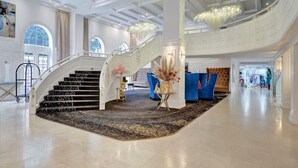 A grand lobby with a central staircase, a chandelier, and a reception area. - Ocean View Condo / Beach Service & Pool / 618 (Miami Beach)