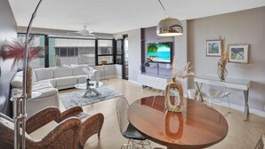 A modern living room with a large TV, a dining area with a wooden table, and a sofa. - Ocean View Condo / Beach Service & Pool / 618 (Miami Beach)