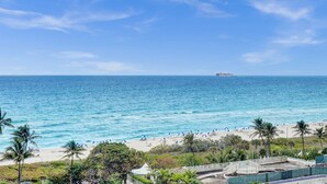 Una playa con agua azul cristalina, palmeras y un barco a lo lejos.