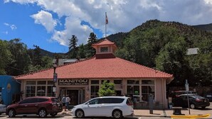Un bâtiment avec un toit recouvert de tuiles rouges, une enseigne indiquant « Manitou Outpost Gallery », et un mât sur lequel flotte le drapeau américain.