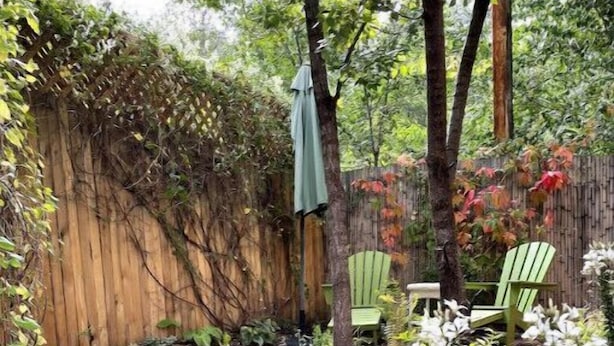 Un chemin de jardin bordé d’une clôture en bois, avec des chaises vertes et des fleurs blanches.