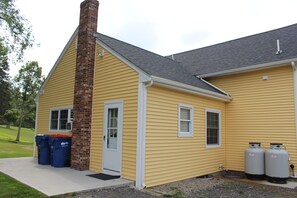 A yellow house with a brick chimney, two propane tanks, and two blue trash bins outside. - Central, Charming & Modern Home (Lakeville)