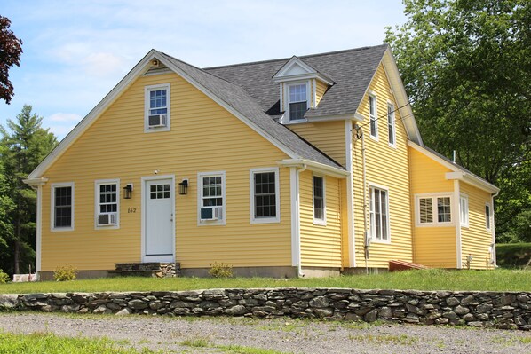 A yellow two-story house with a stone foundation, a front porch, and a small attached garage. - Central, Charming & Modern Home (Lakeville)