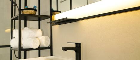 A modern bathroom with a white sink, black shelving, and a mirror above.