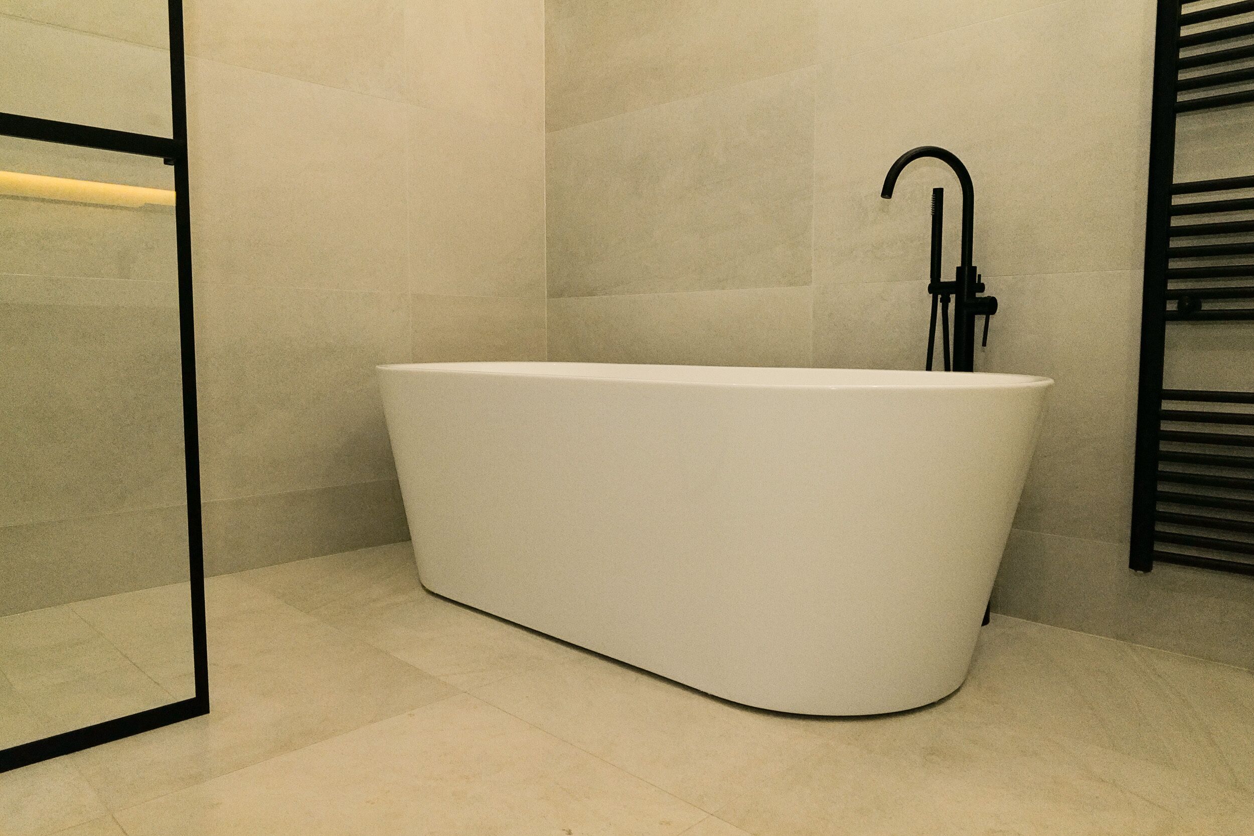 A modern bathroom with a freestanding bathtub, a black faucet, and a tiled floor.