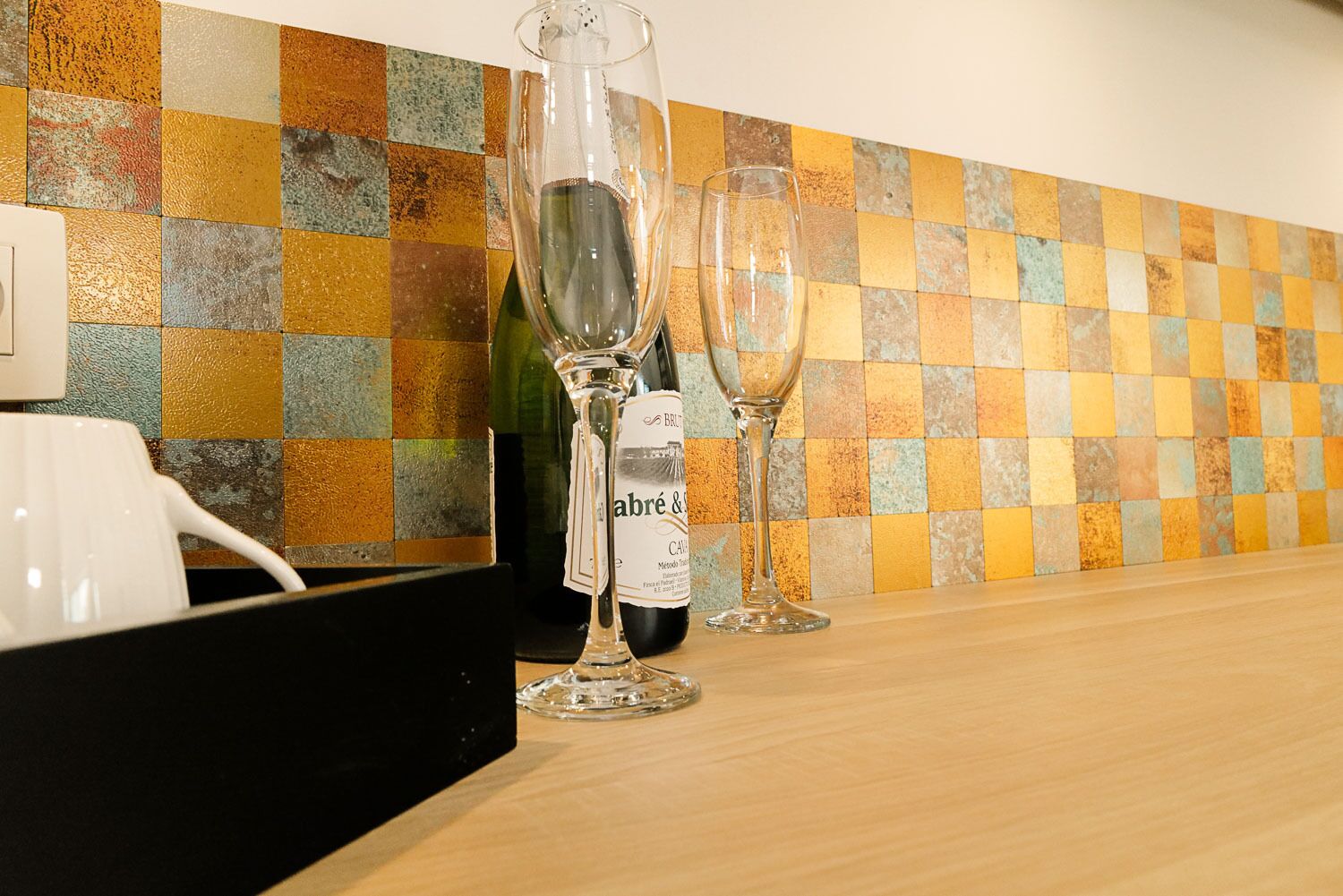 A bar area with a checkered tile backsplash, a wine bottle, and two glasses on a wooden counter.