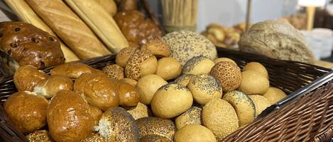 En fletkurv fyldt med forskelligt brød og boller, blandt andet baguette, rundstykker og sesamknækbrød.