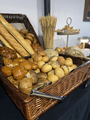 Una cesta de mimbre llena de diferentes tipos de pan y bollos, incluyendo baguettes, panecillos y panes de sésamo.
