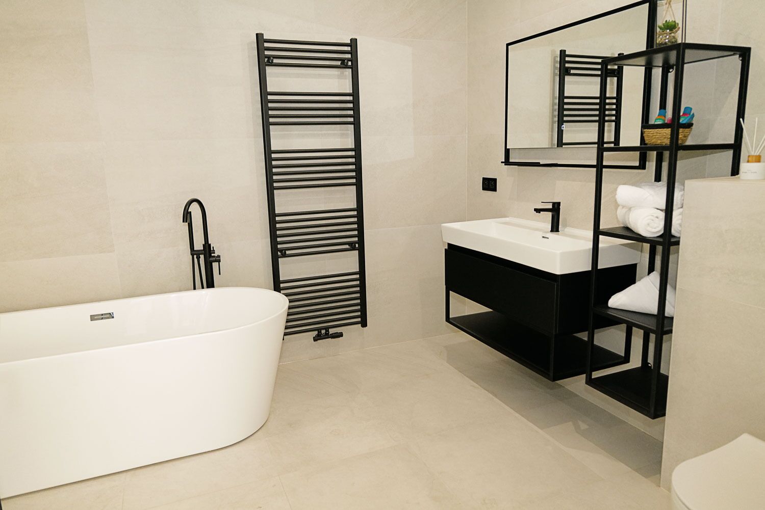 A modern bathroom with a freestanding bathtub, a black towel rack, a white sink, and a black vanity with shelves.