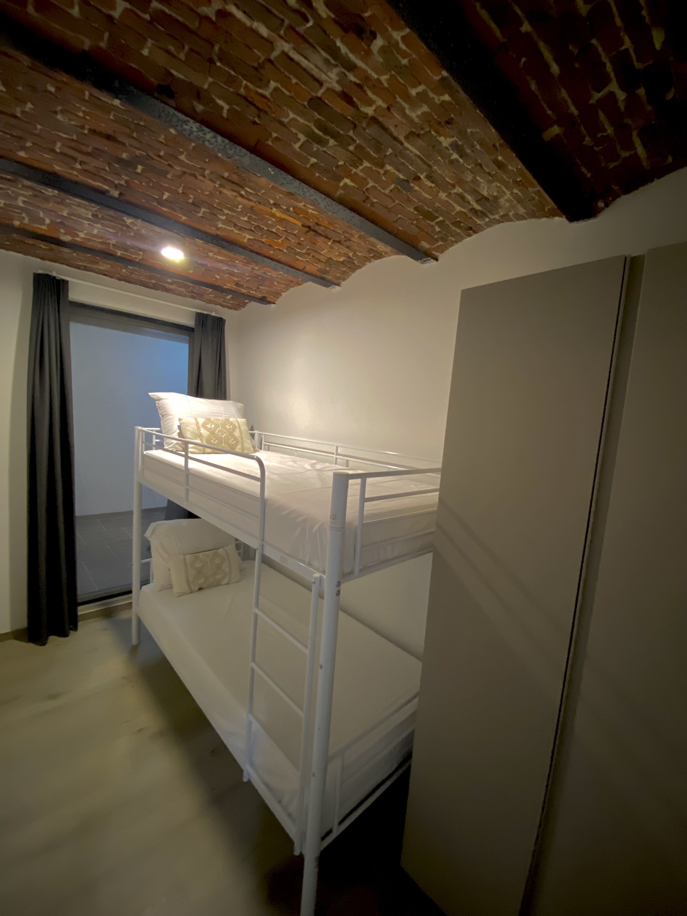 Een stapelbed met een ladder, een deur en een raam met gordijnen.
