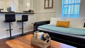 Una sala moderna con un sofá, una mesa de centro y una cocina con armarios blancos y un microondas.