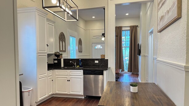 Cocina con armarios blancos, una mesa de comedor de madera y un lavavajillas de acero inoxidable.