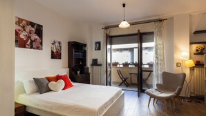 Quarto com cama, cadeira, escrivaninha e vista para o exterior.