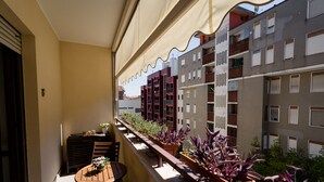 Varanda com mesa, cadeiras, plantas em vasos e vista para edifícios próximos.