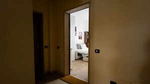 Corredor que dá para um quarto com uma cama, mesa de cabeceira e criado-mudo.