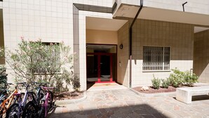 Entrada de um edifício com caminho de pedra que leva a uma porta vermelha.