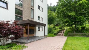 Ein modernes Gebäude mit befestigtem Eingangsbereich, einer kleinen überdachten Fläche und einer Treppe, die zu einer Rasenfläche führt.