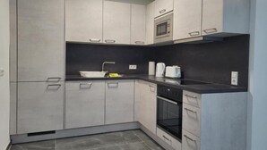Eine moderne Küche mit grauen Schränken, einer schwarzen Arbeitsplatte, einem eingebauten Ofen und einer Mikrowelle.
