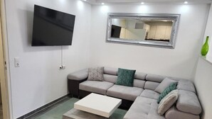 Ein modernes Wohnzimmer mit einer grauen Eckcouch, einem flachbildfernseher an der Wand und einem kleinen Couchtisch.