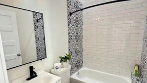 Une salle de bain avec un lavabo, des toilettes et une baignoire blancs, un miroir et des carreaux décoratifs sur les murs.