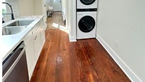 Une buanderie équipée d’un lave-linge et d’un sèche-linge, avec un plancher en bois et des meubles de rangement blancs.
