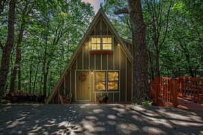 Uma cabana com telhado triangular, varanda frontal e deck de madeira.